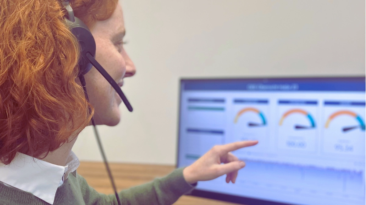 Mitarbeiterin mit Headset zeigt auf ein Dashboard mit Kennzahlen in der smartPLAZA